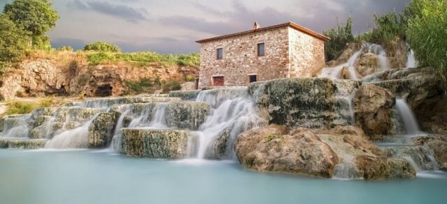 Manantiales termales ricos en azufre que fluyen sobre formaciones rocosas naturales en Italia, ilustrando una fuente natural de azufre y aguas ricas en minerales.