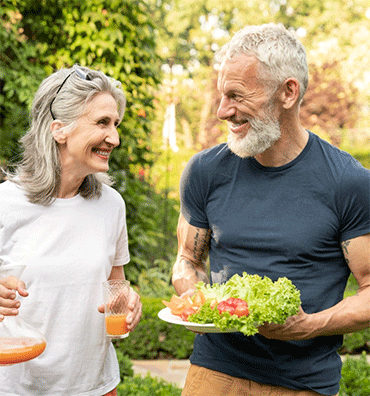 Dos personas mayores compartiendo una ensalada fresca y bebidas al aire libre en un jardín
